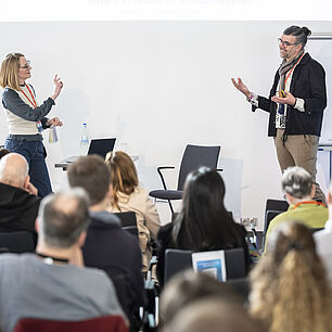 Workshop bei den 20. Münchner AIDS- und Infektiologie-Tagen 2026 in Berlin. Zwei Referenten auf der Bühne. Teilnehmer im Vordergrund.
