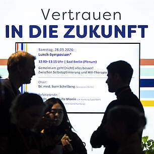 Displayanzeige von Gilead im Ausstellerbereich der 20. Münchner AIDS- und Infektiologie-Tagen 2026 in Berlin. Personen im Vordergrund.